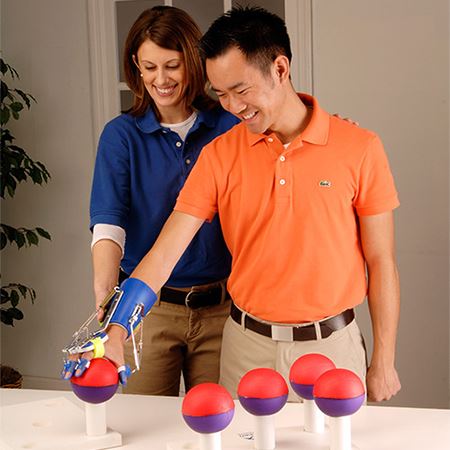 Man in orange shirt using the Saeboflex to pick up therapy balls
