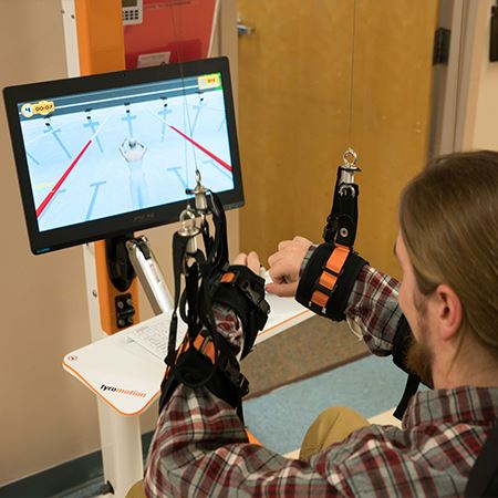 Man using the Tyromotion Diego with straps on wrists looking at a screen